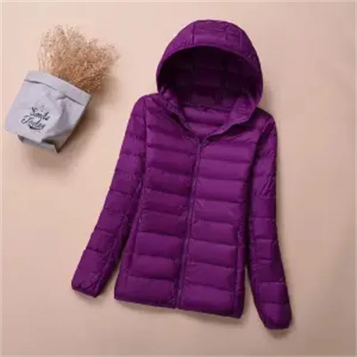 Front view of a purple hooded lightweight puffer jacket with a zipper, next to dried flowers in a bag