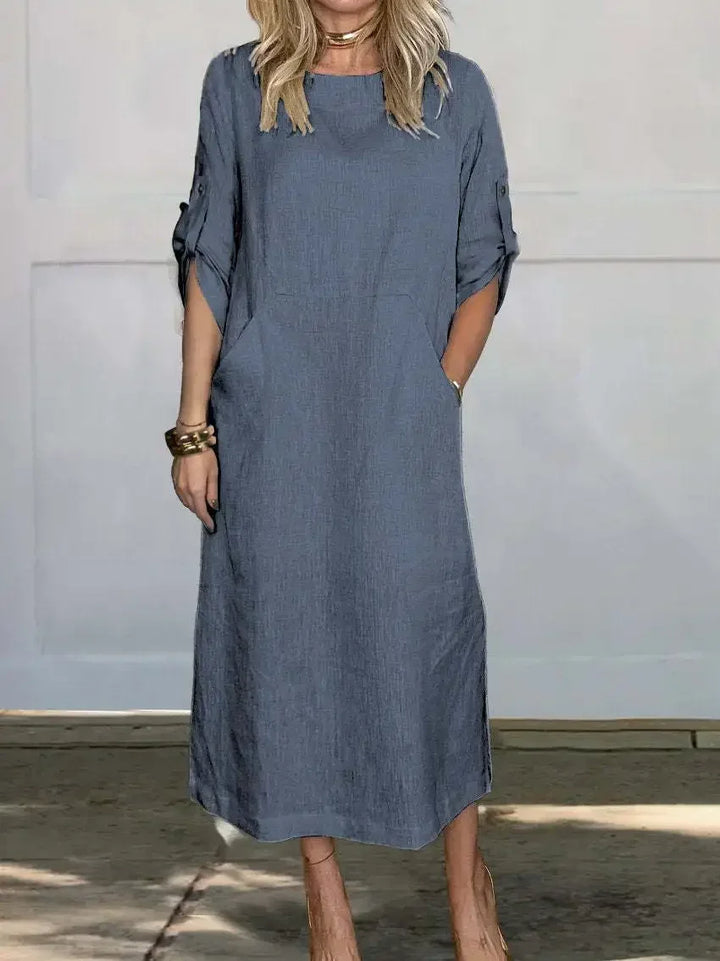 Front view of a woman modelling the Emma Linen Midi Dress with hands in pockets and rolled short sleeves