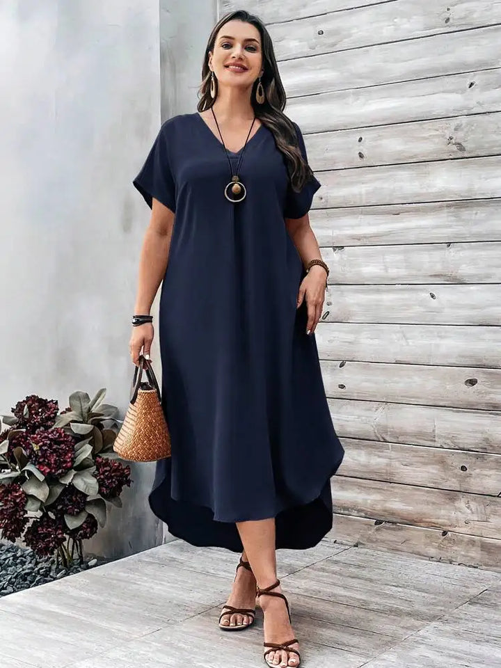 Front view, worn by model, of a plus size V-neck casual dress in navy with a high-low hem and sandals