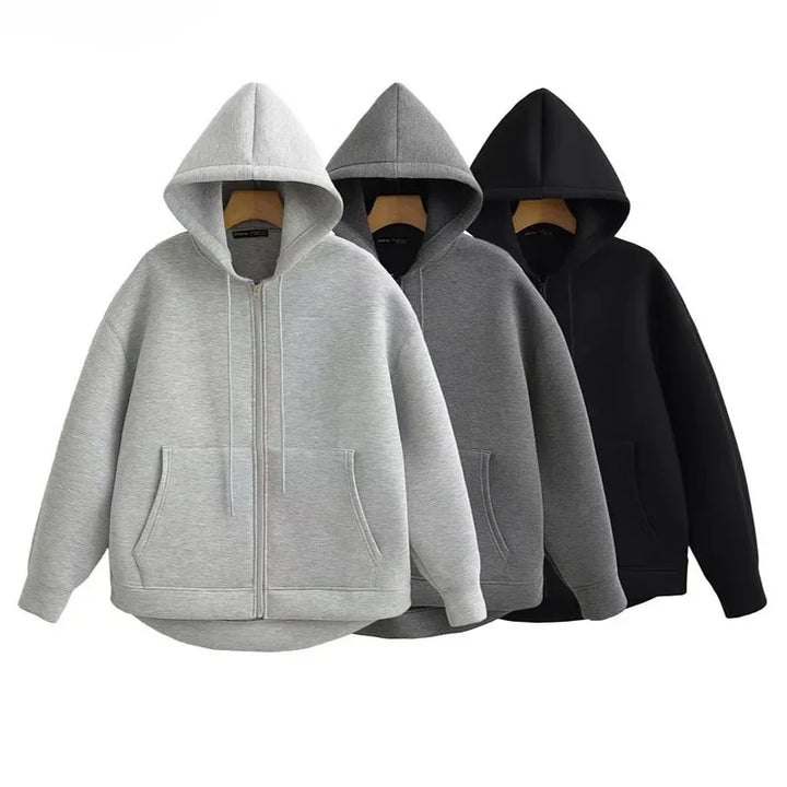 Front view of three oversized full zip hoodies in light grey, dark grey, and black on hangers