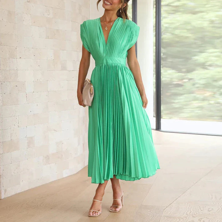 Front view, model wearing a light green Felicia pleated dress with a deep V neckline and cap sleeves