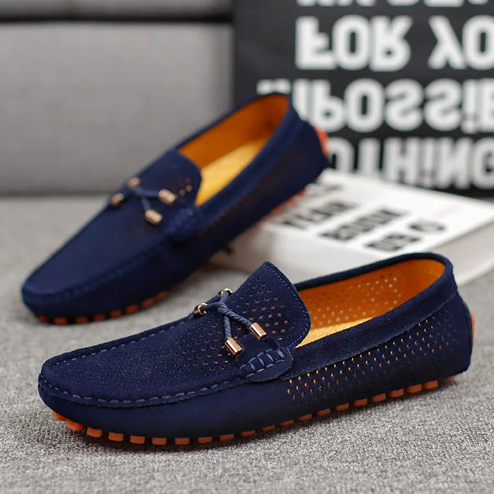 Close up of a navy blue Austin slip-on loafer with perforated detail, orange sole, and decorative bow