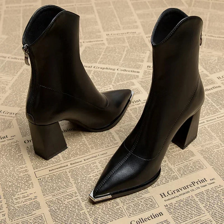 Three quarter view of two black leather Chelsea boots with chrome-tipped pointed toes and block heels