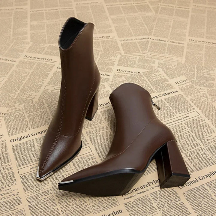 Close up of two brown leather Chelsea boots with chrome-tipped pointed toes and block heels