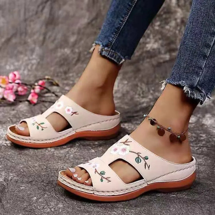 Front view of floral leather slip-on sandals worn by model, showing both feet with an anklet and distressed jeans
