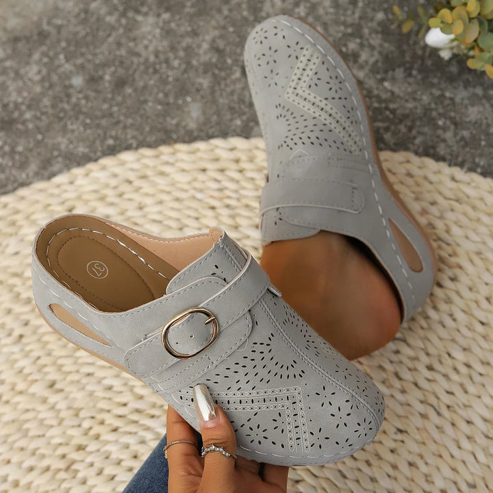 Close up of grey orthopaedic summer slides with perforated detail and a gold buckle, one worn by model