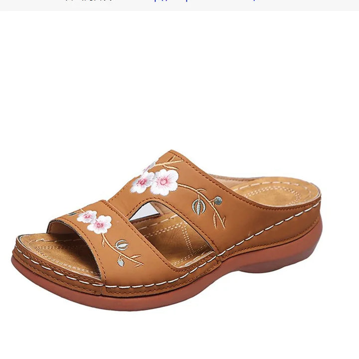 Side view of a single floral leather slip-on sandal with white stitching and a brown sole