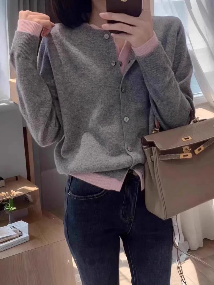 Front view worn by model, a dark grey cashmere cardigan with pink trim over a pink top and dark jeans