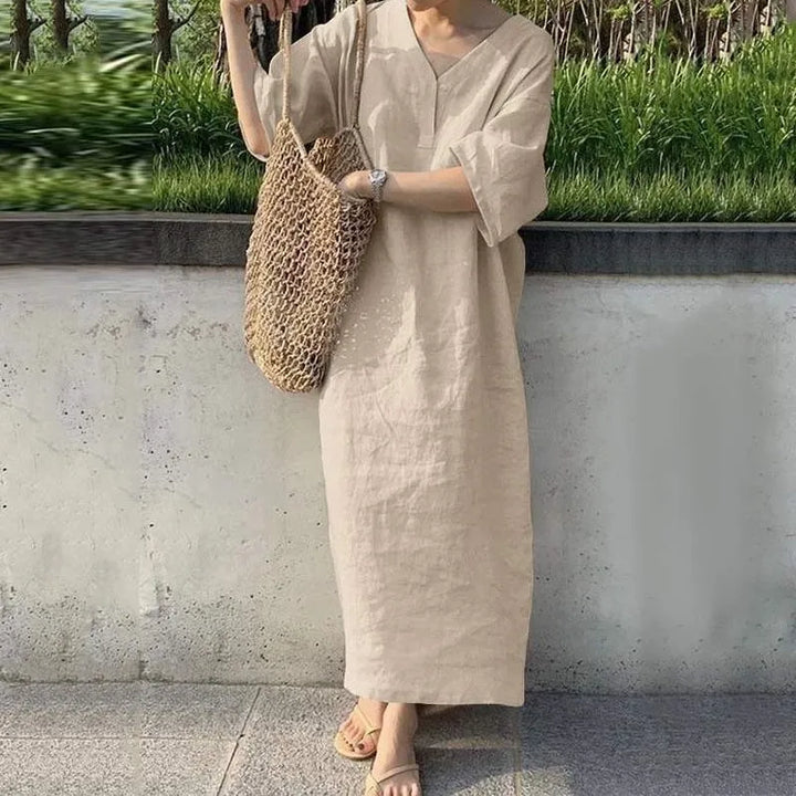 Front view, model wearing the cotton linen V-neck maxi dress in natural with a woven net bag and sandals