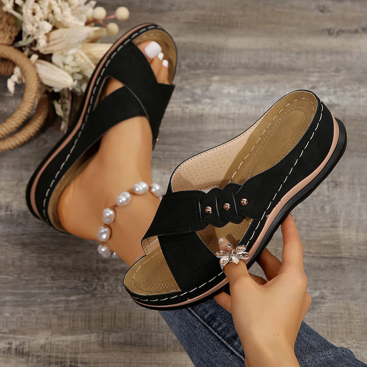 Side view of a model wearing black Gabrielle Summer Slides with a pearl anklet and a hand holding another slide