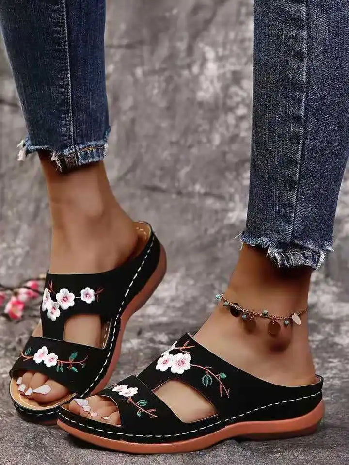 Close up of floral leather slip-on sandals worn by model, showing both feet with an anklet and distressed jeans, closer view