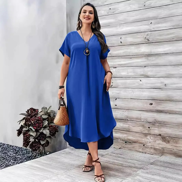 Front view, worn by model, of a plus size V-neck casual dress in royal blue with a woven bag and sandals