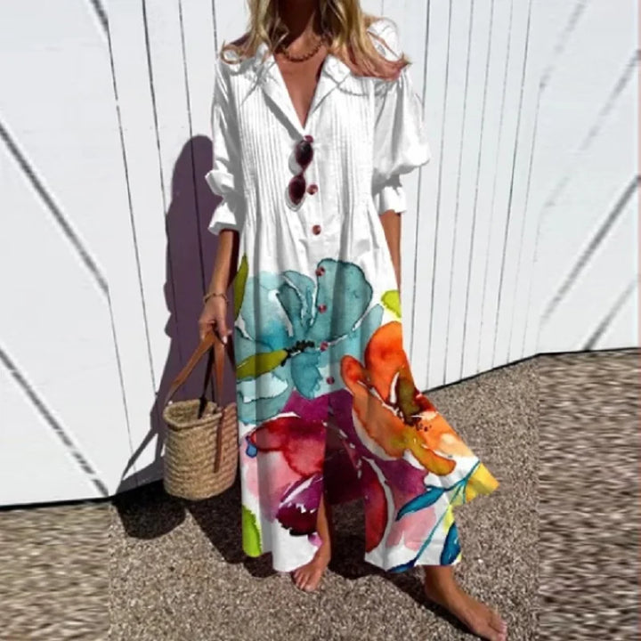 Front view of a model wearing the elegant pleated printed dress with a vibrant watercolour floral pattern and a straw bag