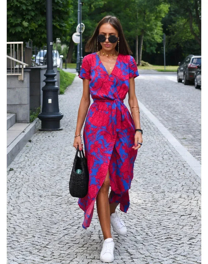 Front view of a model wearing a floral midi dress with a side slit, white sneakers, and a black woven bag