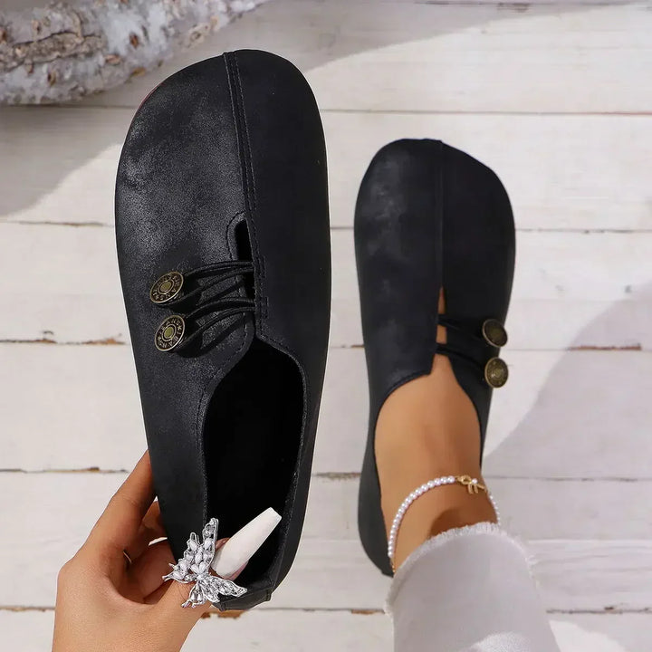 Top view of black soft suede loafers with decorative buttons, one held by hand and one worn by model