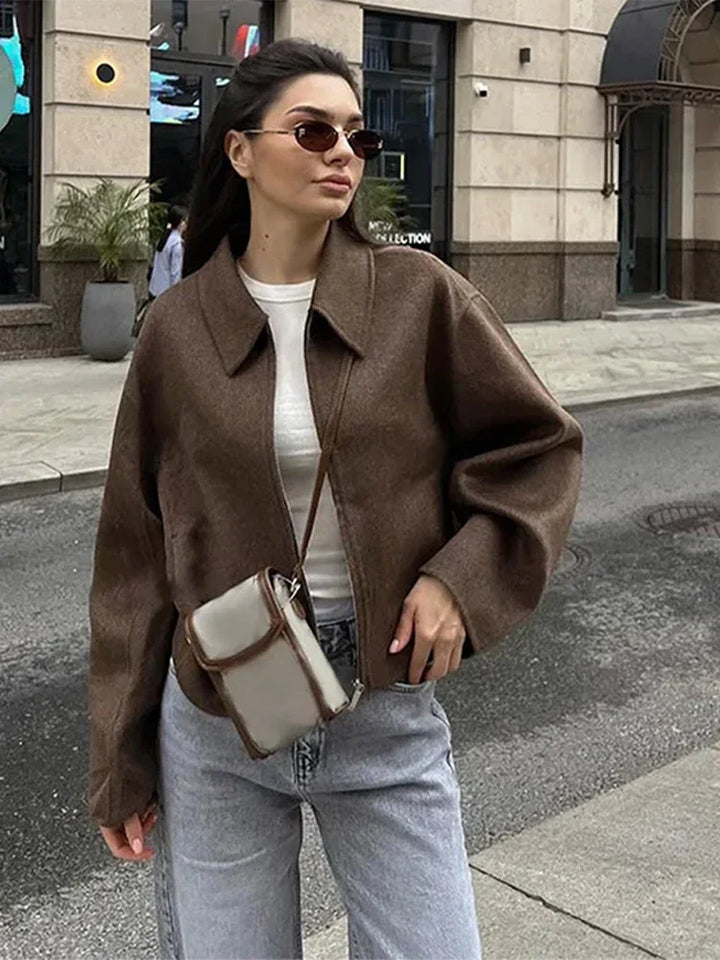 Three quarter view, model wearing a brown Vivienne woolen zip-up jacket with a white top and grey jeans