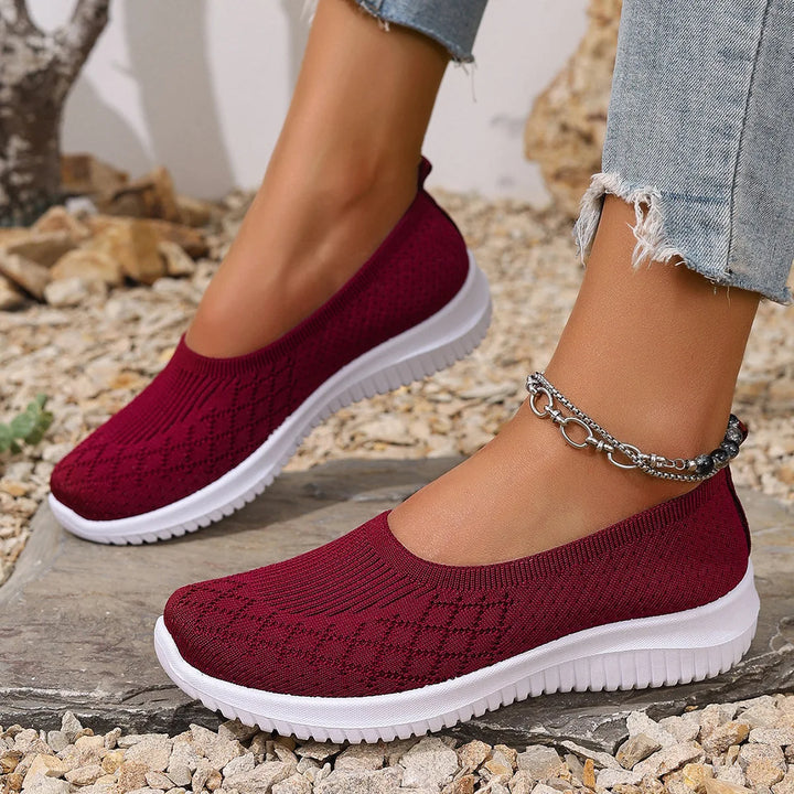 Close up of a model wearing maroon breathable mesh flats with white soles and a silver ankle bracelet
