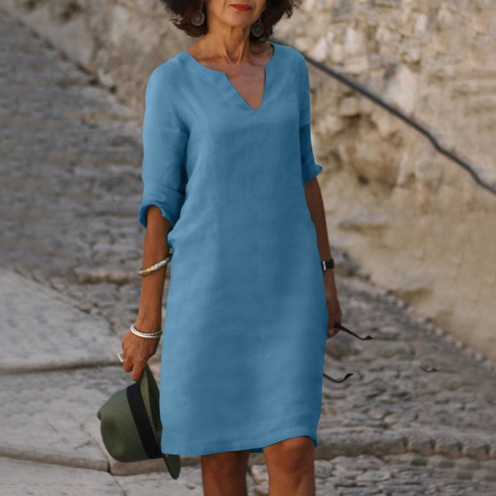 Front view of a woman wearing a blue vintage solid mini dress with three-quarter sleeves, holding a hat