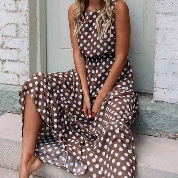 Dotted maxi dress, worn by model, sitting on steps with one bare leg showing, front three quarter view