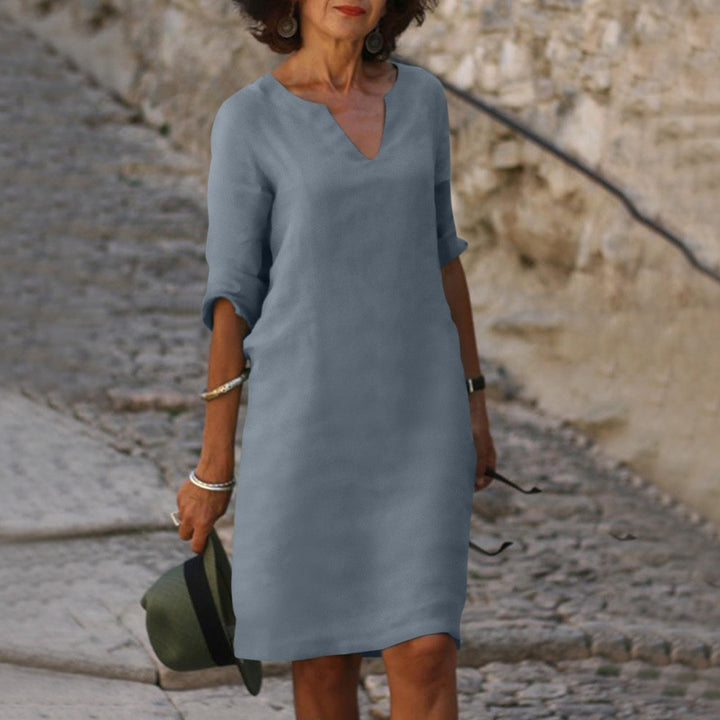 Front view of a woman wearing a blue vintage solid mini dress with three-quarter sleeves, holding a hat, alternate angle
