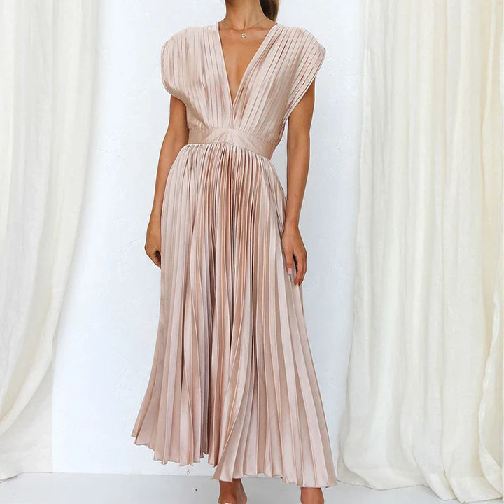 Front view, model wearing a nude Felicia pleated dress with a deep V neckline and cap sleeves