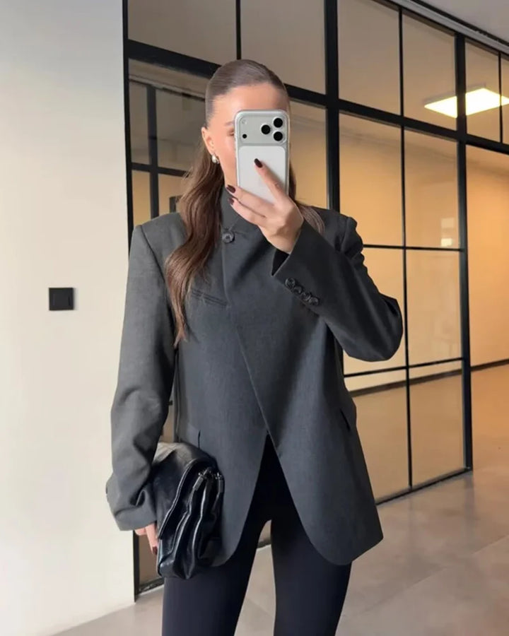 Worn by model, a charcoal grey asymmetric blazer with a single button closure and split back hem