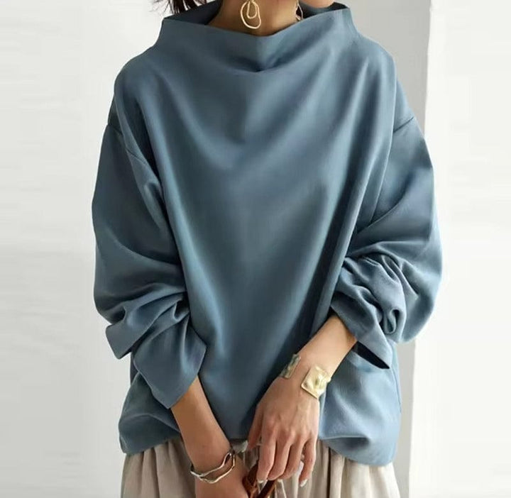 Front view of a model wearing a blue oversized high neck sweater with gathered sleeves and gold jewellery