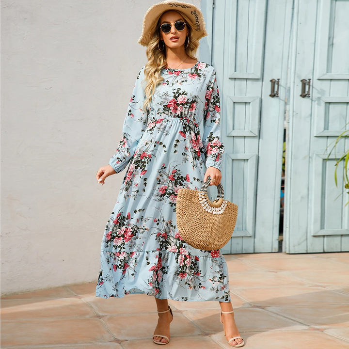 Front view, worn by model, a light blue bohemian chiffon maxi dress with pink floral print, straw hat, and bag