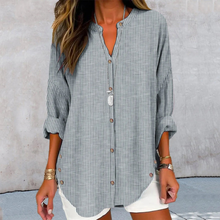 Front view of a model wearing the Kaia printed button blouse in grey and white stripes with a long necklace
