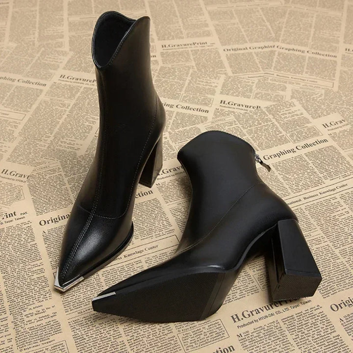 Back view of two black leather Chelsea boots with chrome-tipped pointed toes and block heels