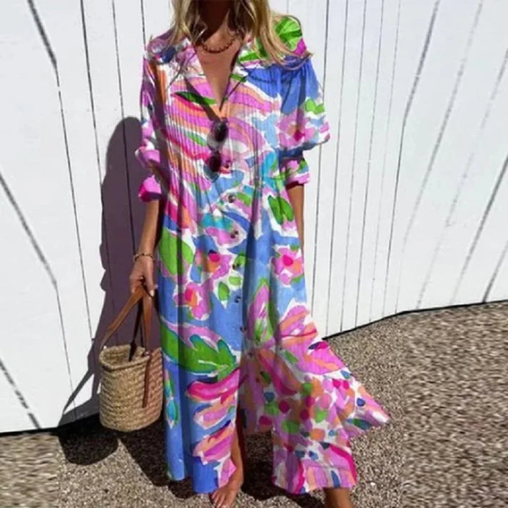 Front view of the elegant pleated printed dress worn by a model, featuring a colourful abstract pattern and a straw bag