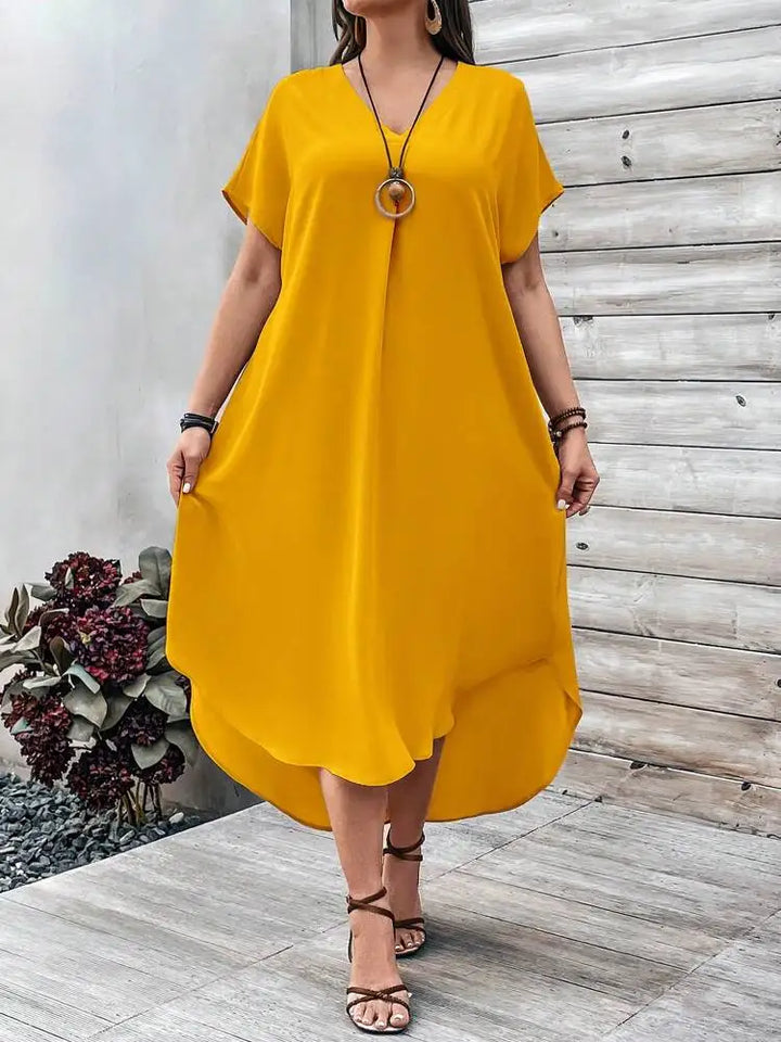 Front view, worn by model, of a plus size V-neck casual dress in mustard with a high-low hem and sandals