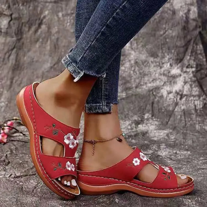 Close up of floral leather slip-on sandals worn by model, showing both feet with an anklet and distressed, alternate angle