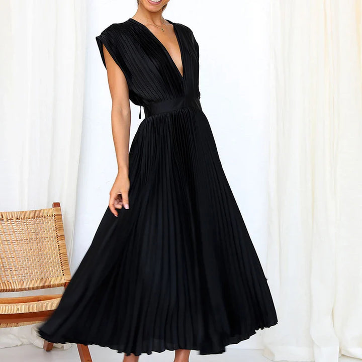 Front view, model wearing a black Felicia pleated dress with a deep V neckline and cap sleeves