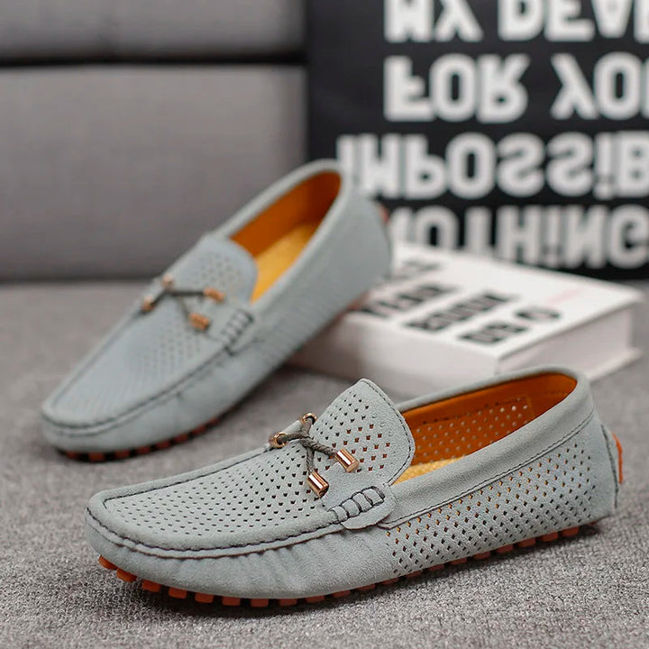 Pair of grey Austin slip-on loafers with perforated detail, orange sole, and decorative bow