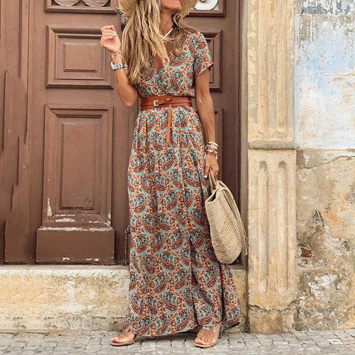 Close up of the floral pleated midi dress worn by a model with a straw hat and woven bag