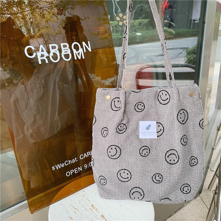 Front view of the Smiley Print Corduroy Tote Bag with a small white tag and gold buttons near the straps
