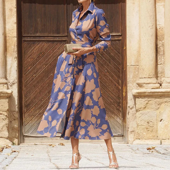 Front view of a model wearing a blue and tan floral midi shirt dress with a tie waist and gold heels