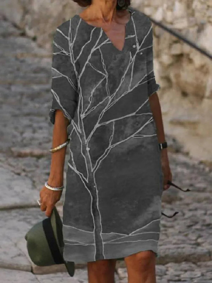 Three quarter view worn by model of a grey vintage printed summer dress with a white tree design