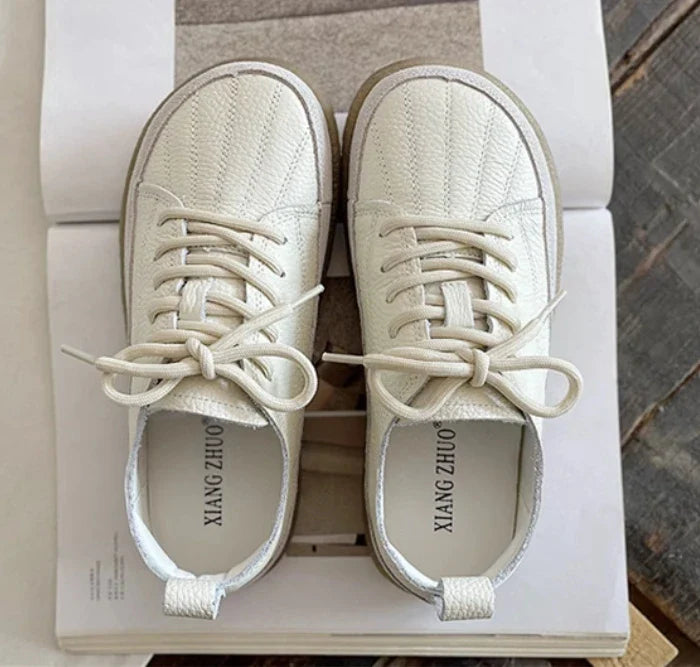 Top down view of a pair of Nora genuine leather flats in cream with cream laces and brown soles