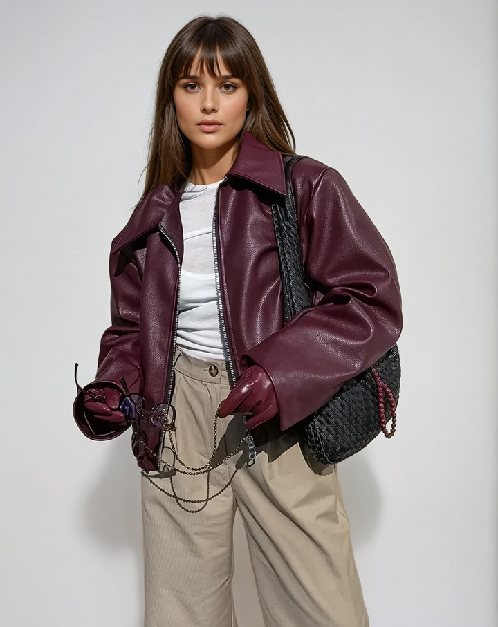Front view of a model wearing a vegan leather jacket, holding a chain with glasses and a handbag