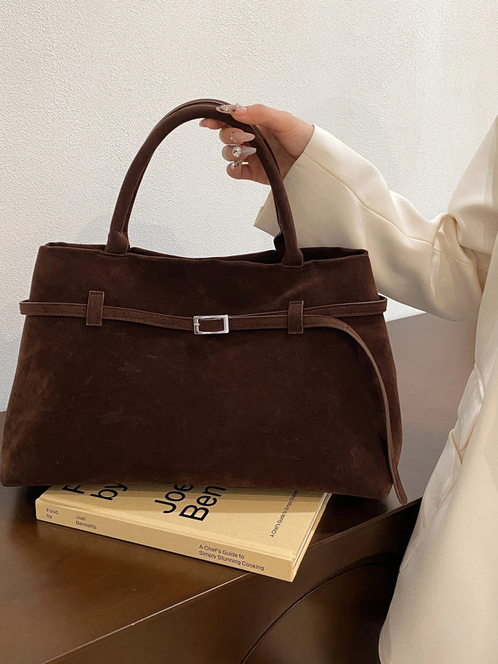 Front view of the Vera Suede Crossbody Handbag in dark brown with a silver buckle detail, held by a model