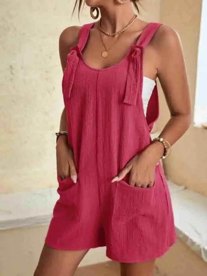 Front view of a woman wearing a casual sleeveless summer romper in berry with tie straps and front pockets