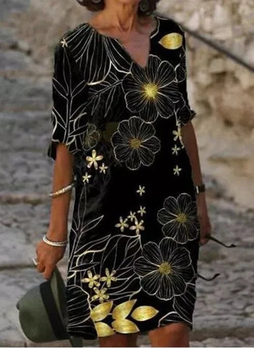 Front view worn by model of a black vintage printed summer dress with gold floral and leaf pattern