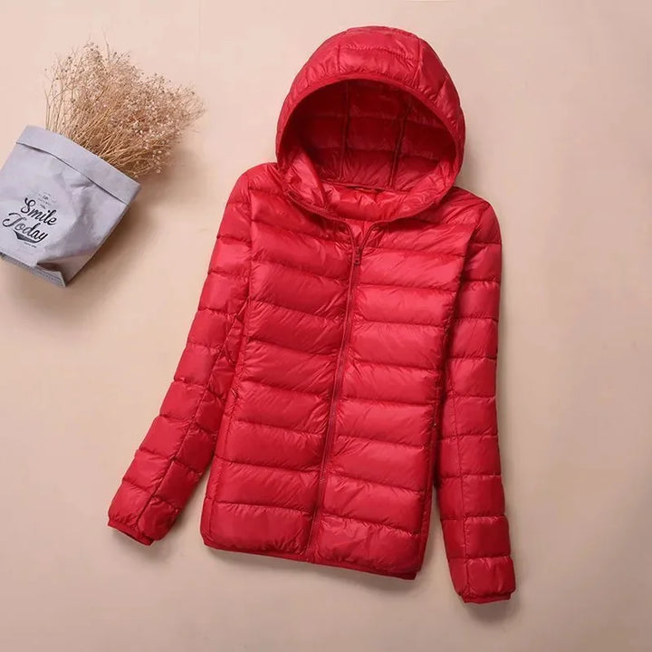 Front view of a red hooded lightweight puffer jacket with a zipper, next to dried flowers in a bag