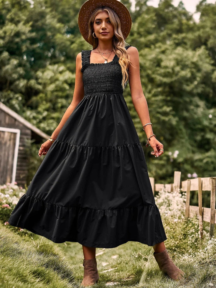 Front view of a model in a black sleeveless halter maxi dress with a square neckline and straw hat