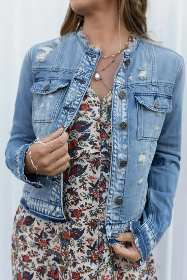 Close up of a model wearing a light blue fitted denim jacket over a floral dress, showing distressed details