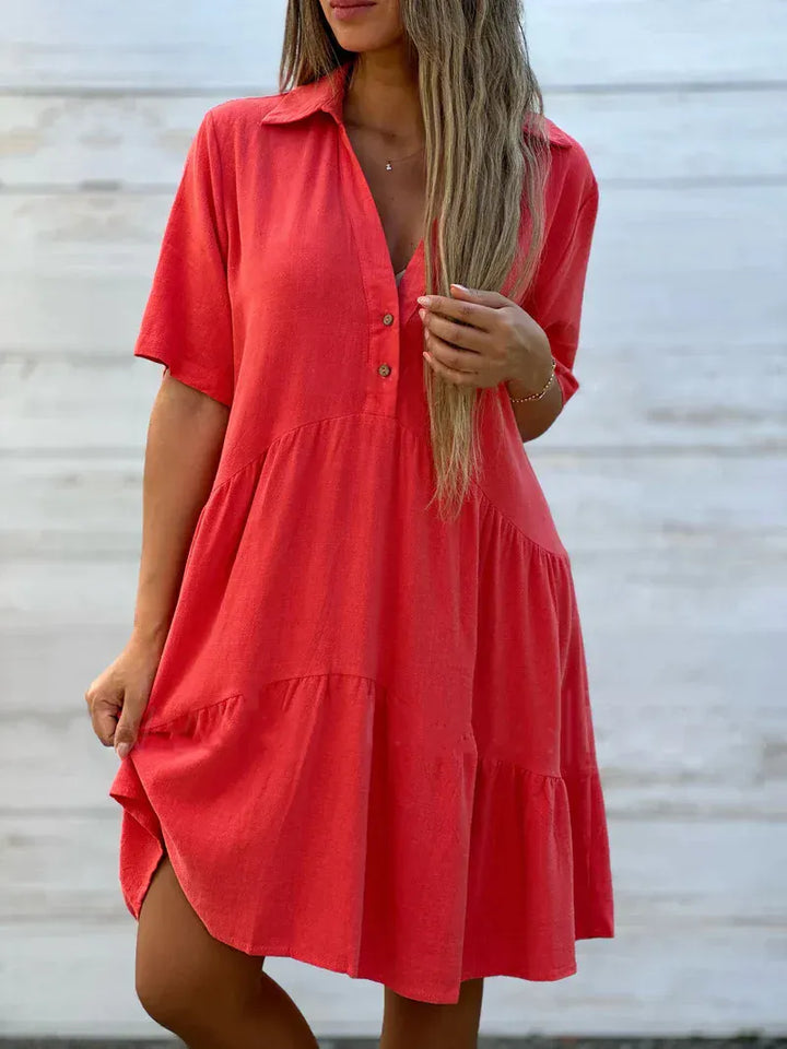 Close up of a model wearing a coral loose blouse mini dress with a collared V-neck and tiered skirt