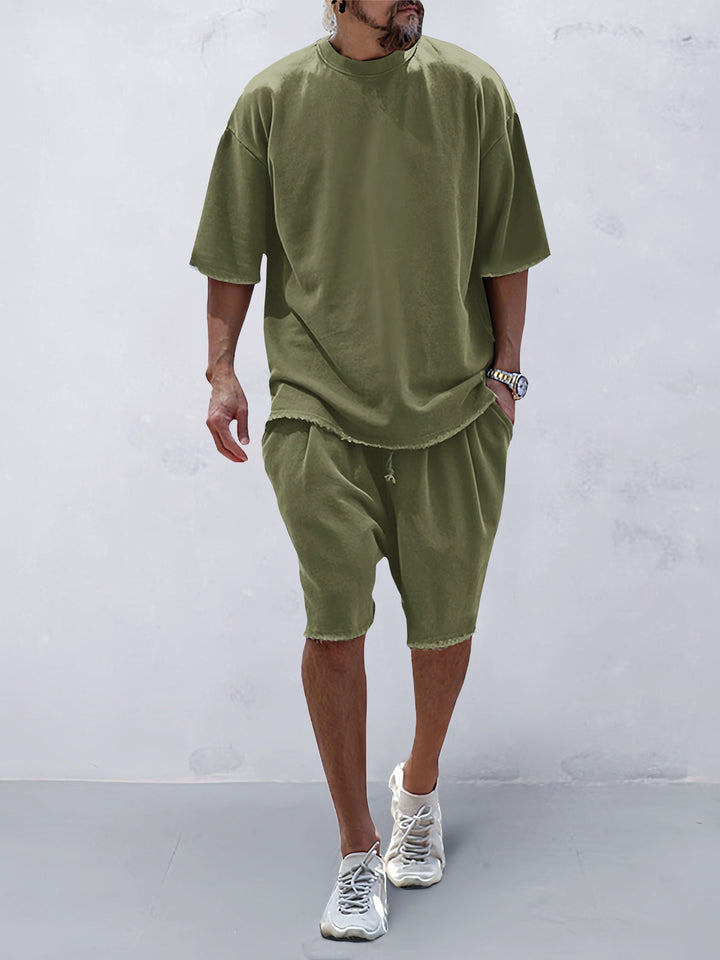 Front view of a model wearing an olive green relaxed fit shorts and matching t-shirt with raw edge hems