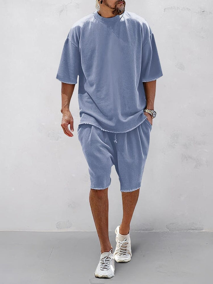 Front view of a model wearing a blue relaxed fit shorts and matching t-shirt with raw edge hems